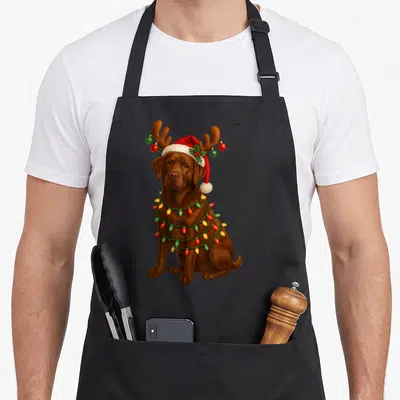 Tablier de cuisine noir avec un labrador chocolat portant une casquette de Père Noël et des lumières festives.
