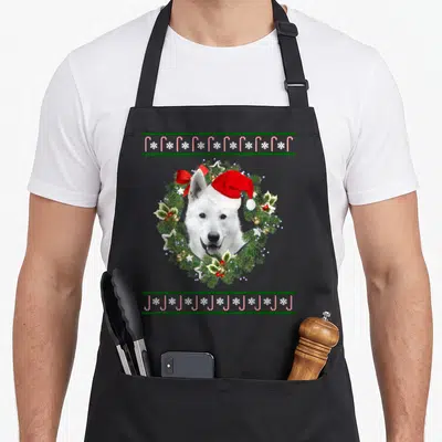 Tablier de cuisine noir avec un chien de berger blanc en couronne de Noël et chapeau de Père Noël.