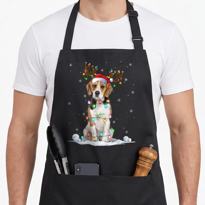 Tablier de cuisine noir avec un beagle portant un chapeau de Père Noël et des antennes de renne illuminées par une guirlande colorée.