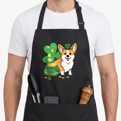 Tablier de cuisine noir avec un corgi portant un chapeau de lutin vert près d'une potée remplie de pièces d'or dorées.