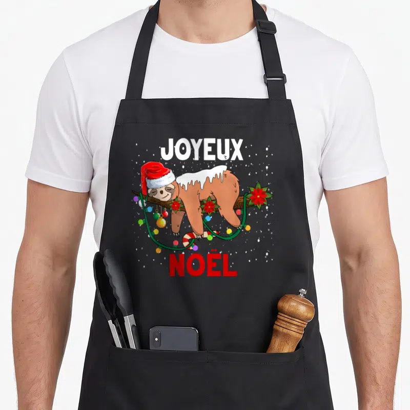 Tablier de cuisine noir avec illustration d'un fourmi paresseux en bonnet de Père Noël accroché à une branche décorée de guirlandes et de fleurs rouges.
