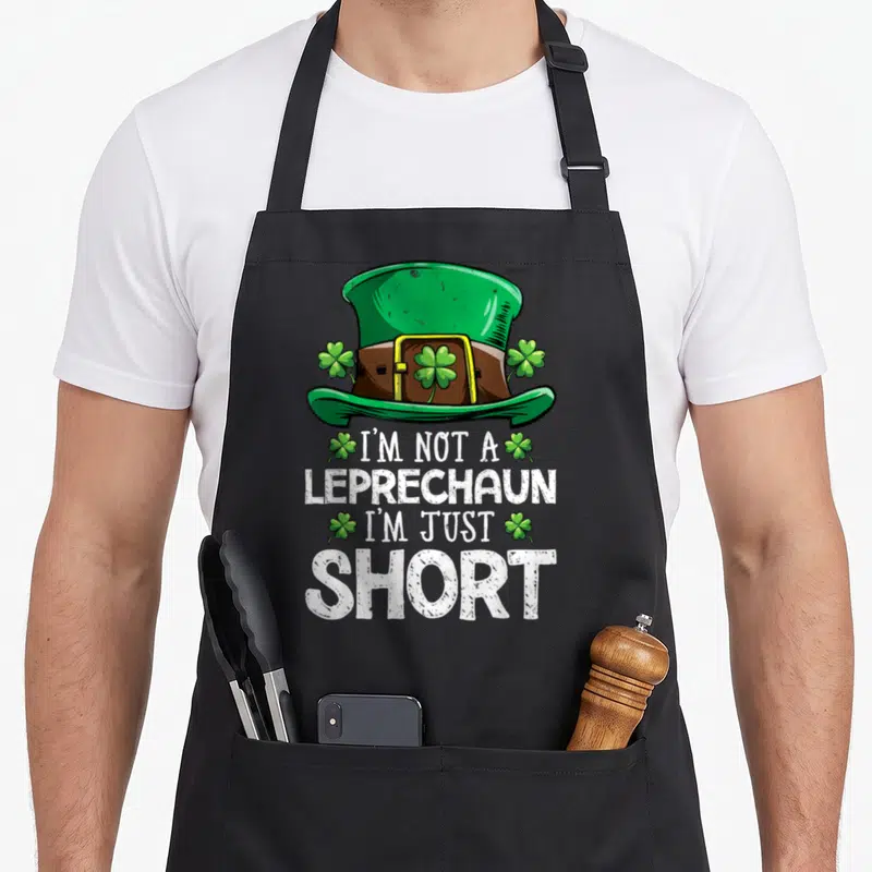 Tablier de cuisine noir avec chapeau vert, trèfles et texte blanc humoristique sur le thème des lutins.