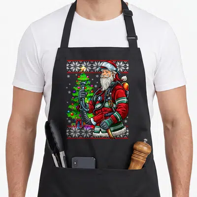 Tablier de cuisine noir avec illustration colorée d'un Père Noël pompier tenant une lance près d'un sapin de Noël.