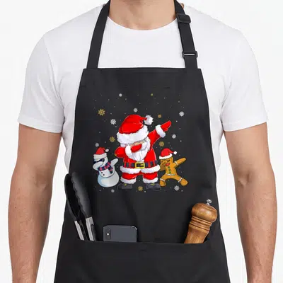 Tablier de cuisine noir avec un Père Noël faisant le dab, un bonhomme de neige aux lunettes de soleil et un biscuit de Noël.