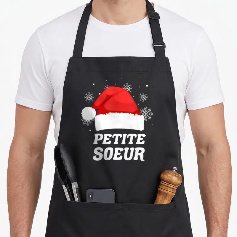 Tablier de cuisine noir avec chapeau Père Noël rouge et texte PETITE SOEUR en blanc.