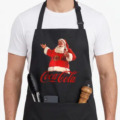Tablier de cuisine noir avec illustration vintage d'un Père Noël tenant une bouteille et le logo Coca-Cola en dessous.