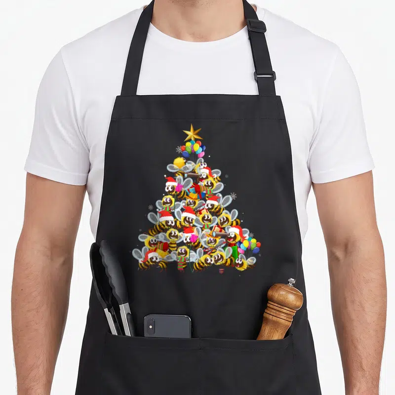 Tablier de cuisine noir avec un motif d'arbre de Noël constitué d'abeilles souriantes portant des chapeaux de Père Noël et tenant des cadeaux.
