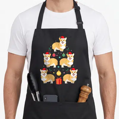 Tablier de cuisine noir avec un sapin de Noël composé de cinq corgis en bonnet rouge et décorations colorées.