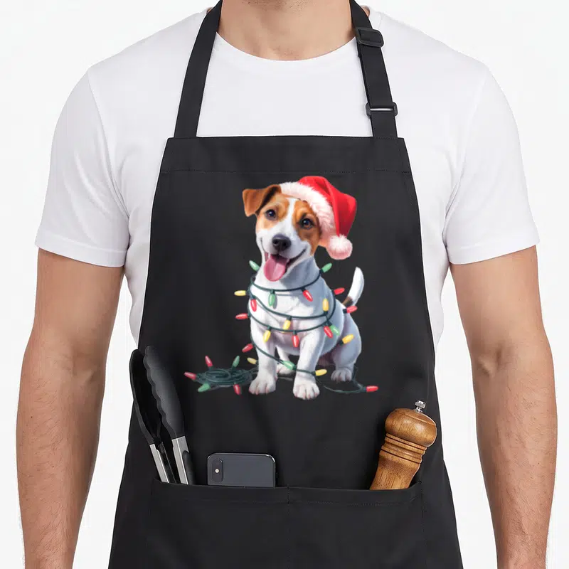 Tablier de cuisine noir avec un chien Jack Russell portant un bonnet de Noël et des lumières festives autour du cou.