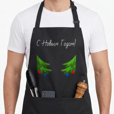Tablier de cuisine noir avec deux arbres de Noël verts et une inscription en alphabet cyrillique blanc au centre.