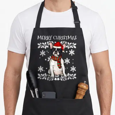 Tablier de cuisine noir avec un Bouledogue Français portant un bonnet rouge et un foulard à carreaux verts et rouges.