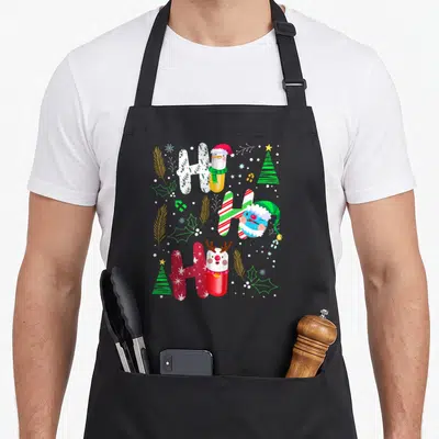 Tablier de cuisine noir avec un motif coloré représentant les mots Ho Ho Ho sous forme de pilules décorées de motifs de Noël.