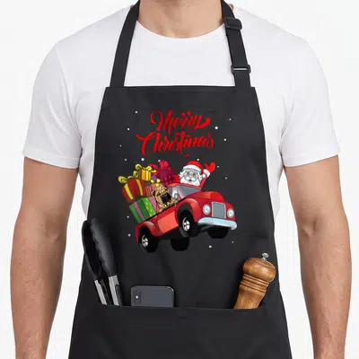 Tablier de cuisine noir avec illustration colorée d'un Père Noël et d'un Shar-Pei dans un camion rouge chargé de cadeaux.