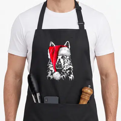 Tablier de cuisine noir avec illustration d'un chien de berger suisse blanc portant une casquette de Père Noël rouge et blanche.