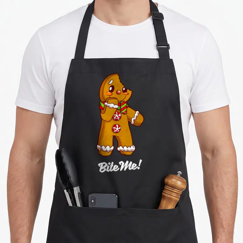Tablier de cuisine noir avec un biscuit gingerbread marron, collier à carreaux et texte Bite Me en bas.
