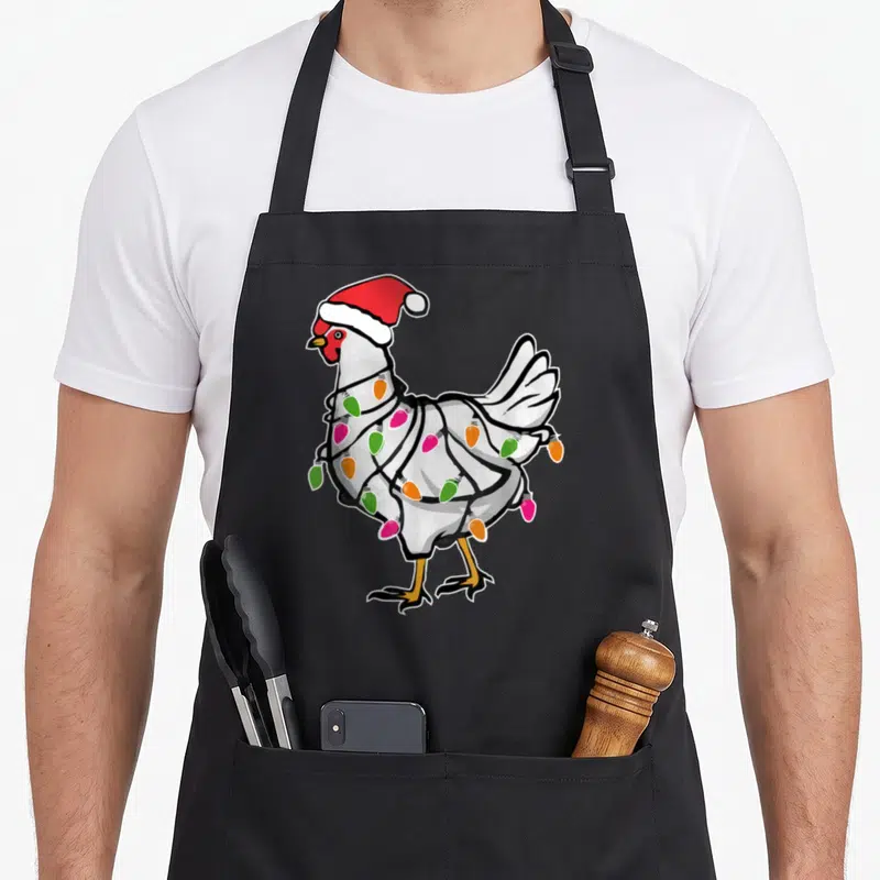 Tablier de cuisine noir avec un poulet blanc coiffé d'un bonnet rouge et enroulé dans des guirlandes colorées.