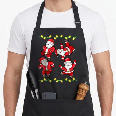Tablier de cuisine noir avec quatre Pères Noël en train de danser et une guirlande lumineuse jaune sur fond gris.