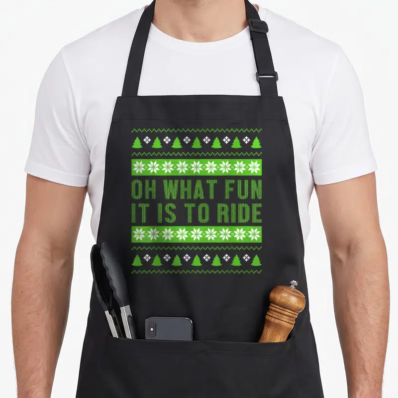 Tablier de cuisine noir avec motif Noël vert Oh What Fun It Is To Ride et motifs de flocons.