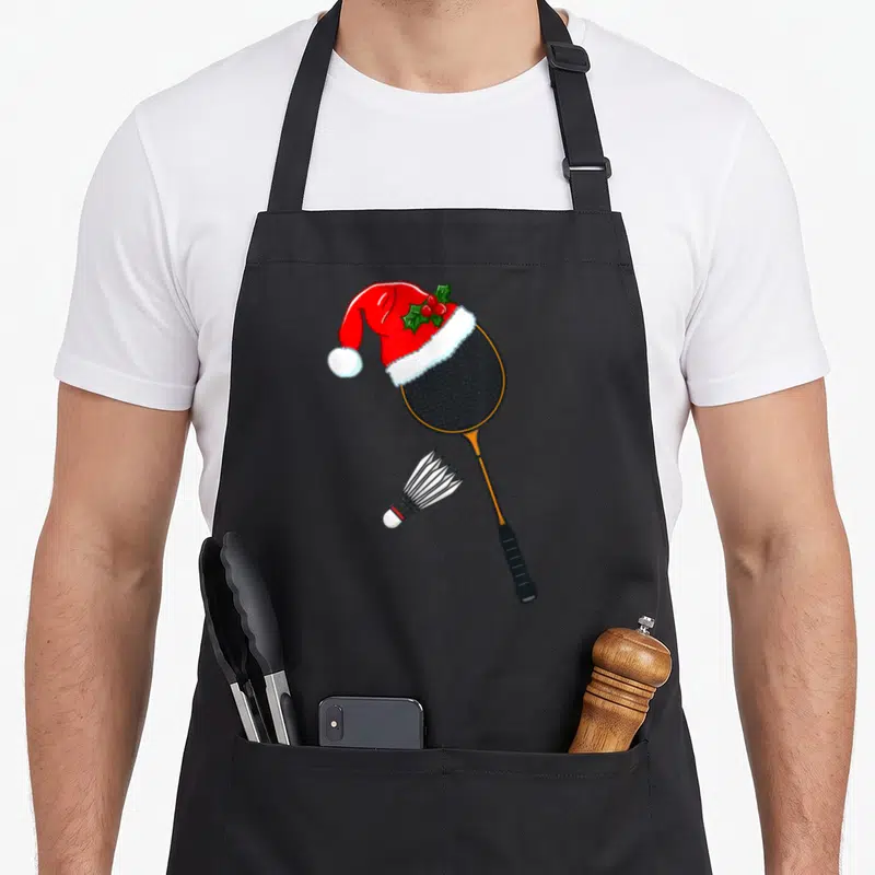 Tablier de cuisine noir avec une raquette de badminton portant un chapeau de Père Noël et un volant en dessous.