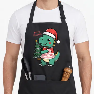 Tablier de cuisine noir avec un dinosaure vert mignon en chapeau de Père Noël tenant un petit sapin de Noël.