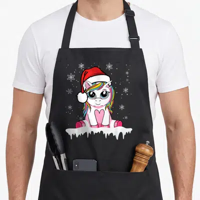 Tablier de cuisine noir avec une licorne rose au bonnet rouge et des flocons blancs autour.