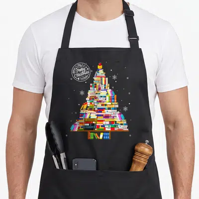 Tablier de cuisine noir avec un arbre de Noël composé de livres colorés et une inscription Merry Christmas en cercle.