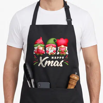 Tablier de cuisine noir avec trois gnomes de Noël tenant des biscuits et le texte Happy Xmas.