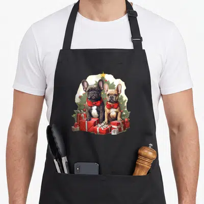 Tablier de cuisine noir avec deux bouledogues français en nœuds papillon rouges devant des cadeaux de Noël.