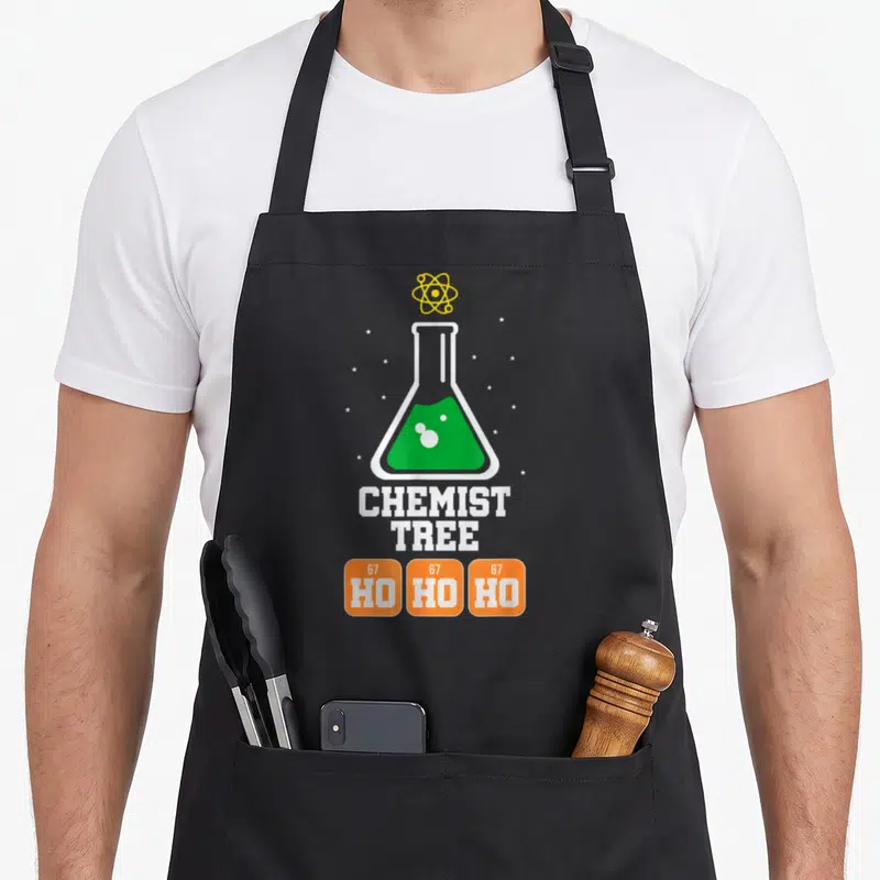 Tablier de cuisine noir avec un flacon à contenu vert, une atomes jaune et le texte Chemist Tree sur fond d'étoiles blanches.