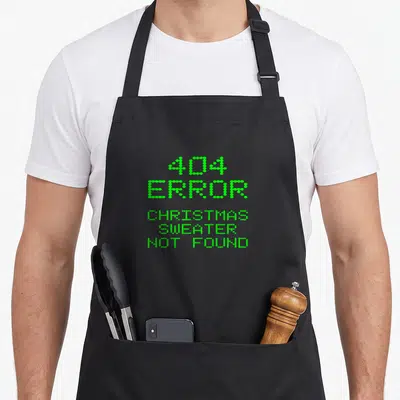 Tablier de cuisine noir avec texte vert pixelisé erreur 404 et message « Christmas sweater not found » centré sur le devant.