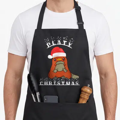 Tablier de cuisine noir avec un dessin coloré d'un animal australien portant un bonnet rouge et le texte Platy Christmas en blanc.