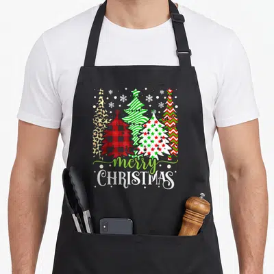Tablier de cuisine noir avec cinq sapins de Noël aux motifs léopard, plaid, étoiles et le texte merry CHRISTMAS en bas.