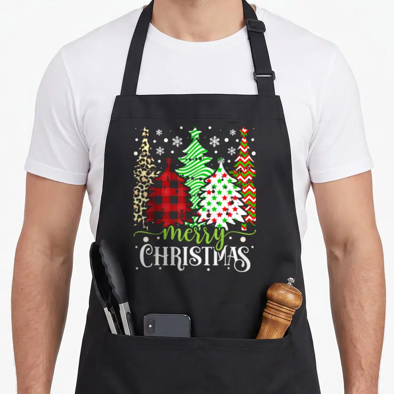Tablier de cuisine noir avec cinq sapins de Noël aux motifs léopard, plaid, étoiles et le texte merry CHRISTMAS en bas.