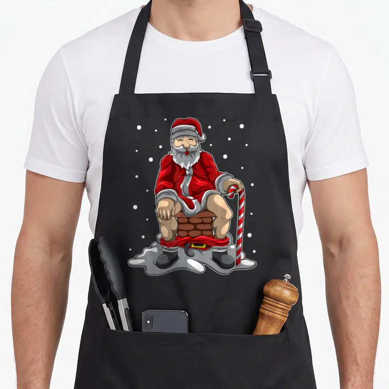Tablier de cuisine noir avec illustration du Père Noël assis sur une cheminée tenant une canne.