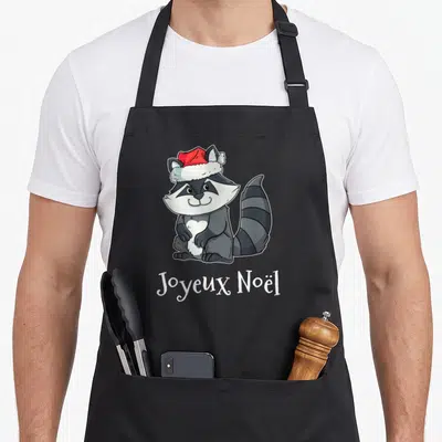 Tablier de cuisine noir avec illustration d'un raton laveur portant un chapeau de Père Noël et le texte Joyeux Noël en dessous.