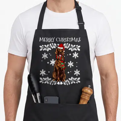 Tablier de cuisine noir avec illustration d'un setter irlandais portant un bonnet de Père Noël et une écharpe à carreaux rouge et vert.