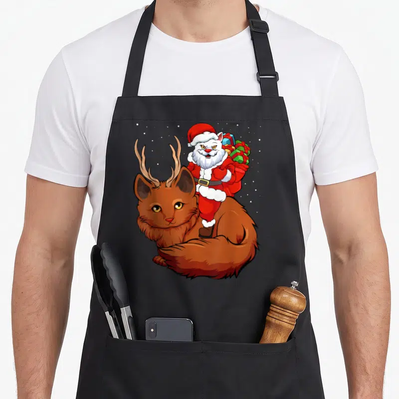 Tablier de cuisine noir avec illustration d'un Père Noël sur un renne chaton aux yeux dorés sous la neige.