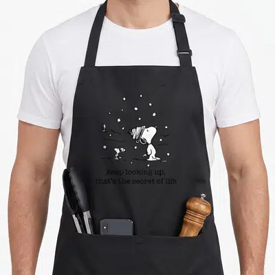 Tablier de cuisine noir avec Snoopy et Woodstock sous la neige et le texte keep looking up that's the secret of life