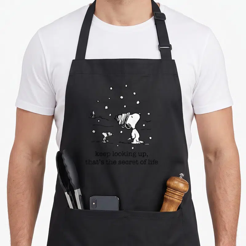 Tablier de cuisine noir avec Snoopy et Woodstock sous la neige et le texte keep looking up that's the secret of life