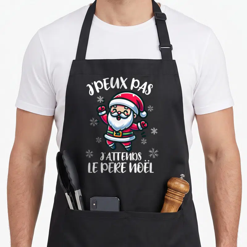 Tablier de cuisine noir avec illustration colorée d'un Père Noël sautant et texte blanc J'peux pas j'attends le Père Noël