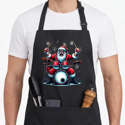 Tablier de cuisine noir avec un Père Noël batteur rock jouant de la batterie sous des paillettes de neige stylisées.