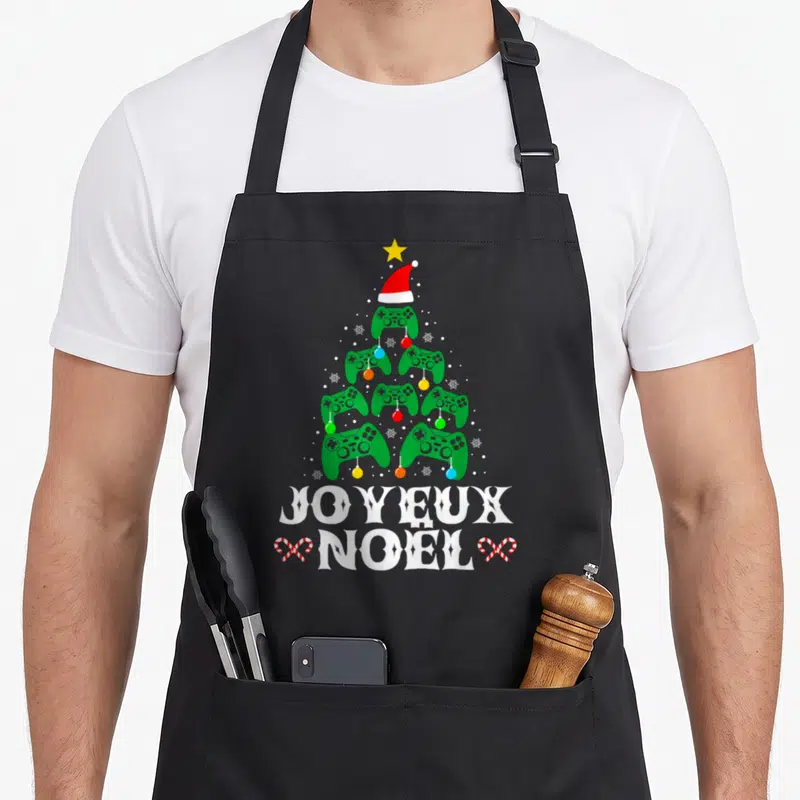 Tablier de cuisine noir avec un arbre de Noël formé de manettes vertes et l'inscription Joyeux Noël en blanc.