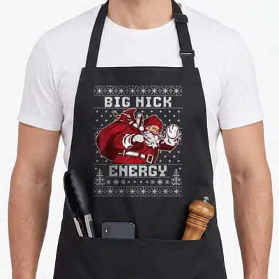 Tablier de cuisine noir avec illustration Père Noël Big Nick Energy et motifs de tricot blancs.