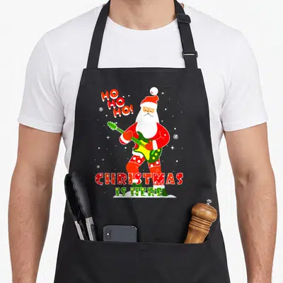 Tablier de cuisine noir avec un Père Noël jouant de la guitare verte et le texte Christmas is Here.