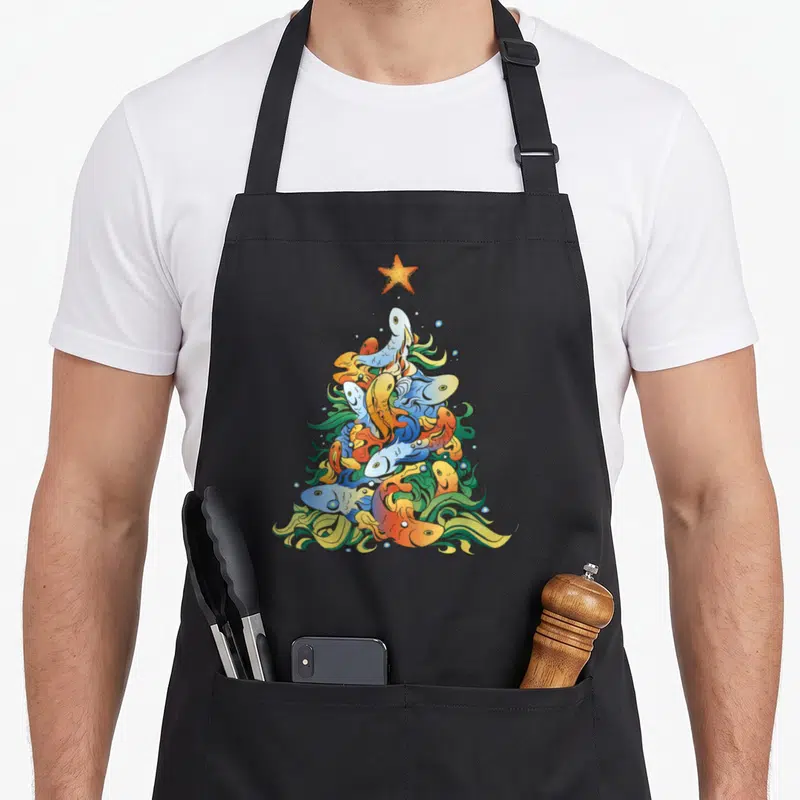 Tablier de cuisine noir avec un sapin de Noël composé de poissons colorés et d'une étoile orange en haut.