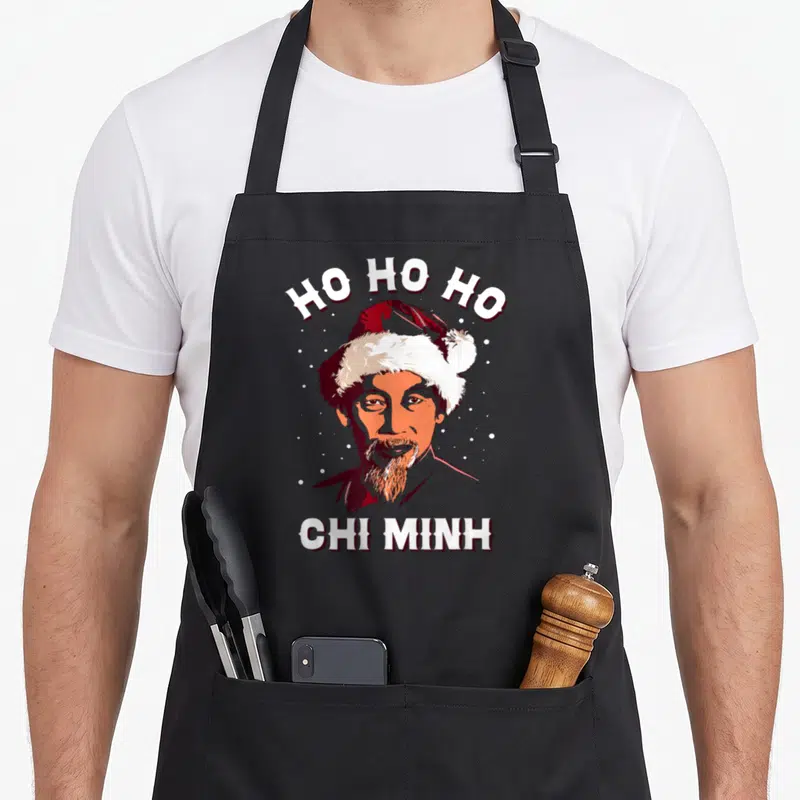 Tablier de cuisine noir avec portrait stylisé de Ho Chi Minh portant un bonnet de Père Noël et le texte Ho Ho Ho Chi MinH.