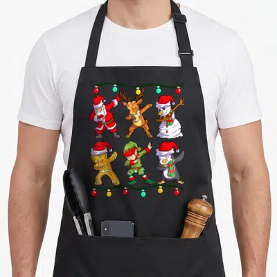 Tablier de cuisine noir avec six personnages de Noël en train de faire le dab sous des lumières festives.