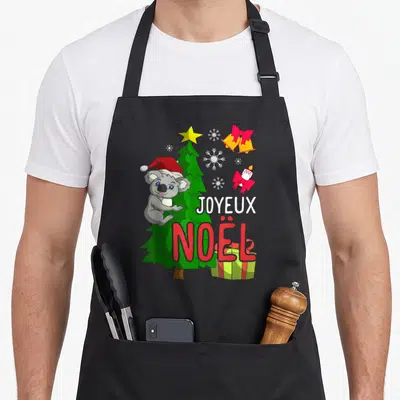 Tablier de cuisine noir avec un koala en bonnet rouge près d'un sapin et l'inscription Joyeux Noël.