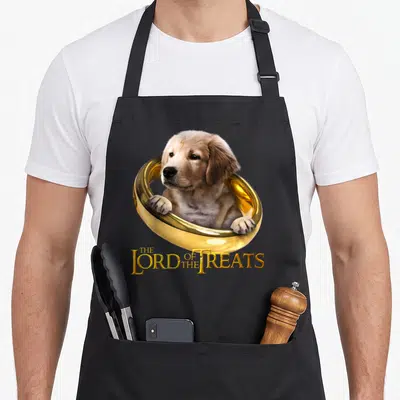 Tablier de cuisine noir avec un chiot golden retriever dans un anneau d'or et le texte The Lord of the Treats en lettres dorées.
