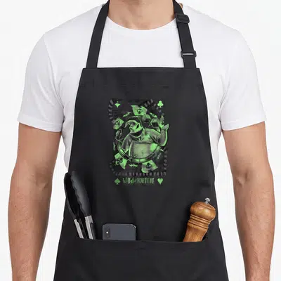 Tablier de cuisine noir avec illustration verte d'Oogie Boogie en carte à jouer et texte Wheel of Fortune en bas.
